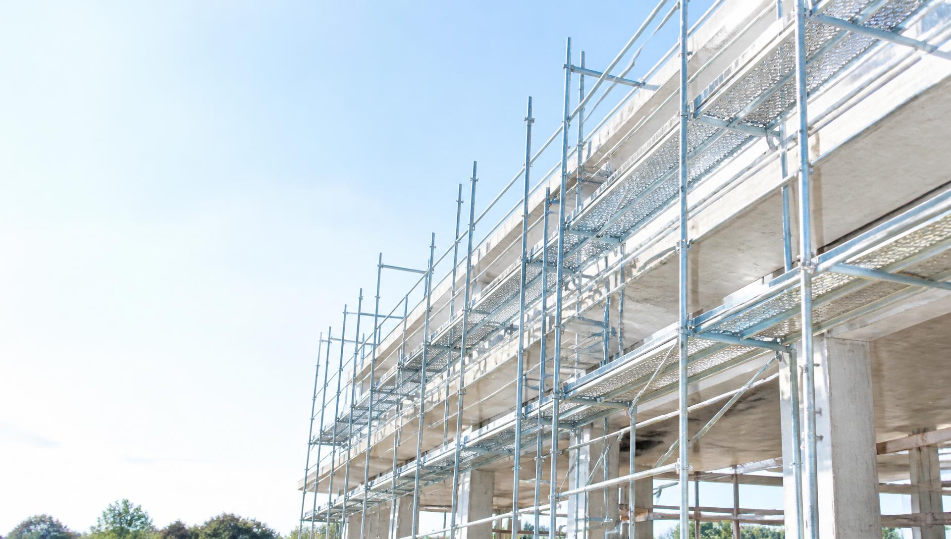 Bright industrial scaffolding erected along a concrete structure under clear daylight
