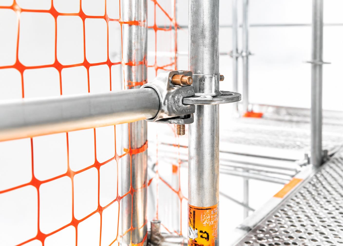 Close view of a scaffold coupler, guardrail tube and orange safety netting in bright daylight